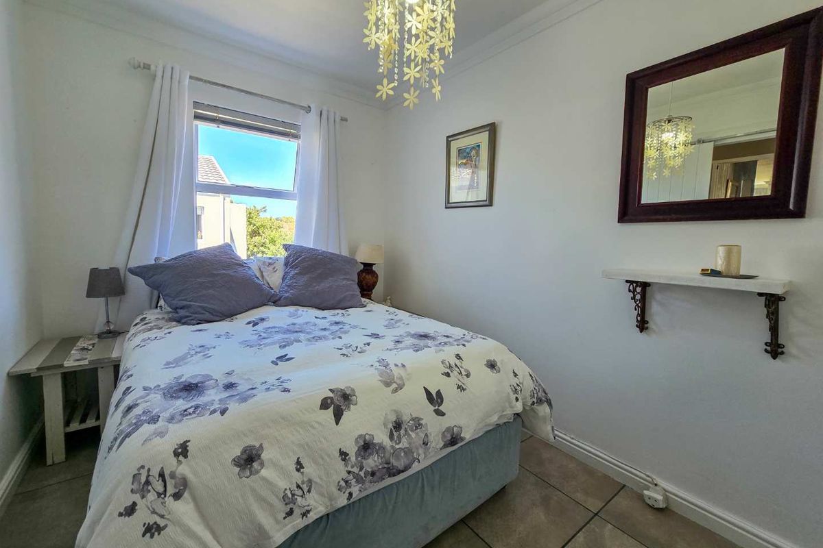 A cozy bedroom featuring tiled flooring, a window with natural light, and a wall-mounted shelf with a mirror.