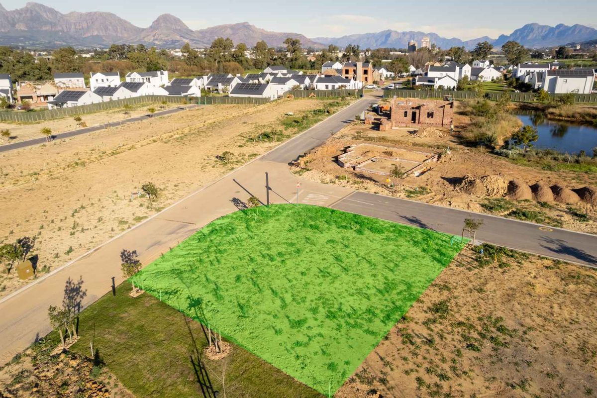 Aerial view of a vacant residential plot in a developed estate, featuring mountain views and established road infrastructure.
