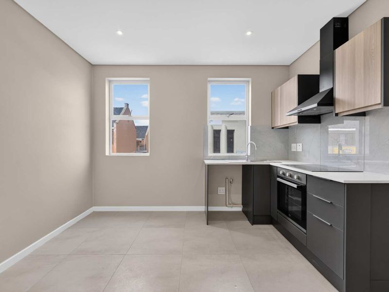 Modern, empty kitchen featuring sleek dark grey and wood-tone cabinetry, stone countertops, integrated oven, hob, and extractor fan with neutral tiled flooring.