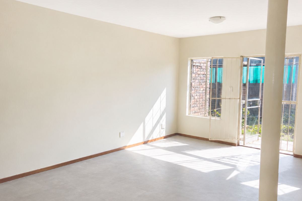 A bright, empty living area featuring neutral tiled flooring, a structural support column, and direct access to the rear exterior through a security gate.