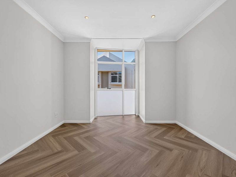 A bright, empty bedroom featuring modern herringbone vinyl flooring, recessed downlighting, and neutral wall finishes.
