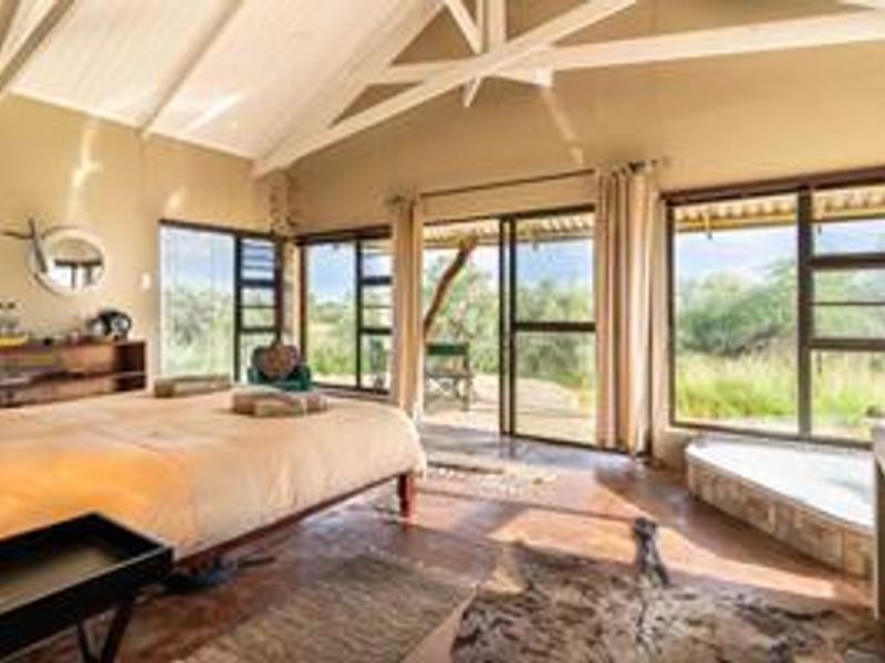Spacious bedroom featuring vaulted ceilings with exposed beams, large windows, and direct access to an outdoor patio area with natural landscape views.