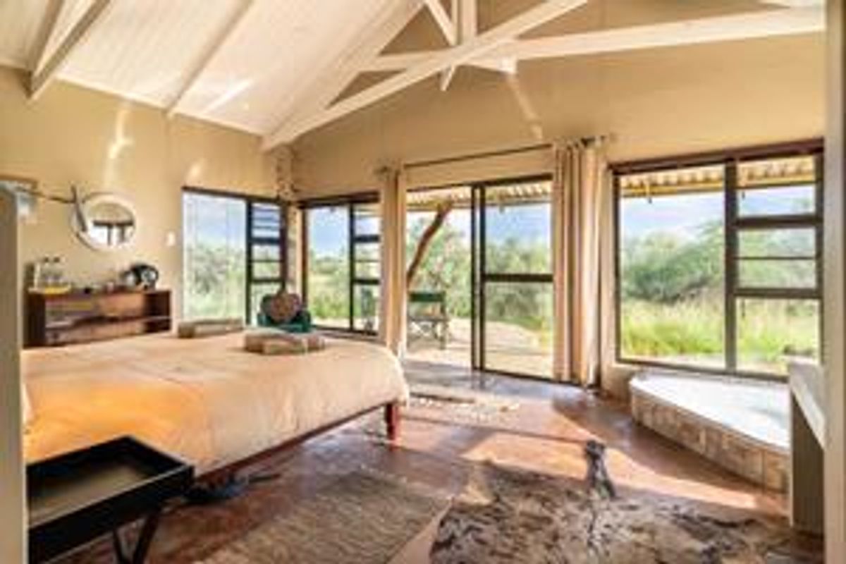 Spacious bedroom featuring vaulted ceilings with exposed beams, large windows, and direct access to an outdoor patio area with natural landscape views.
