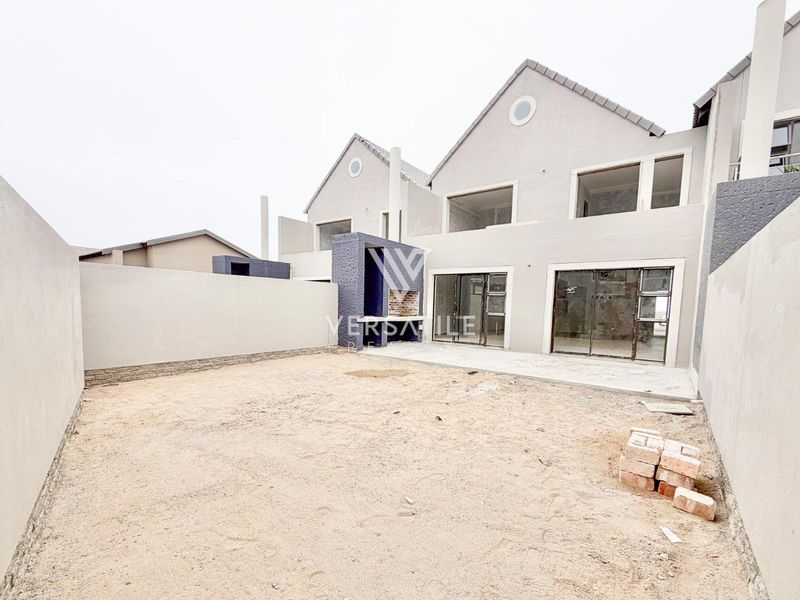 Rear view of a townhouse featuring a paved patio, built-in braai, and an unlandscaped garden space ready for custom design.