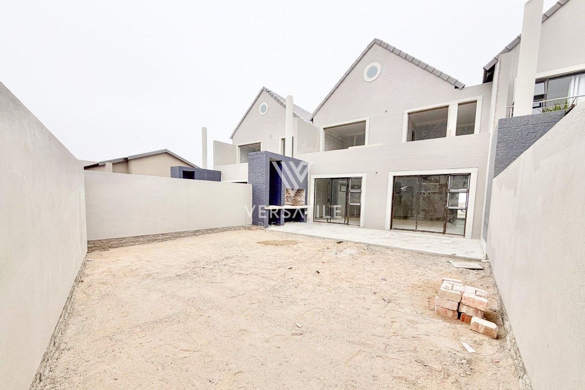 Rear view of a townhouse featuring a paved patio, built-in braai, and an unlandscaped garden space ready for custom design.