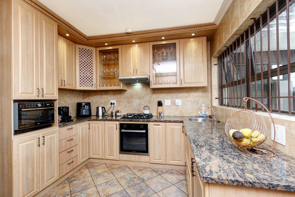 A well-maintained kitchen featuring light wood cabinetry, granite countertops, built-in appliances, and tiled finishes throughout.