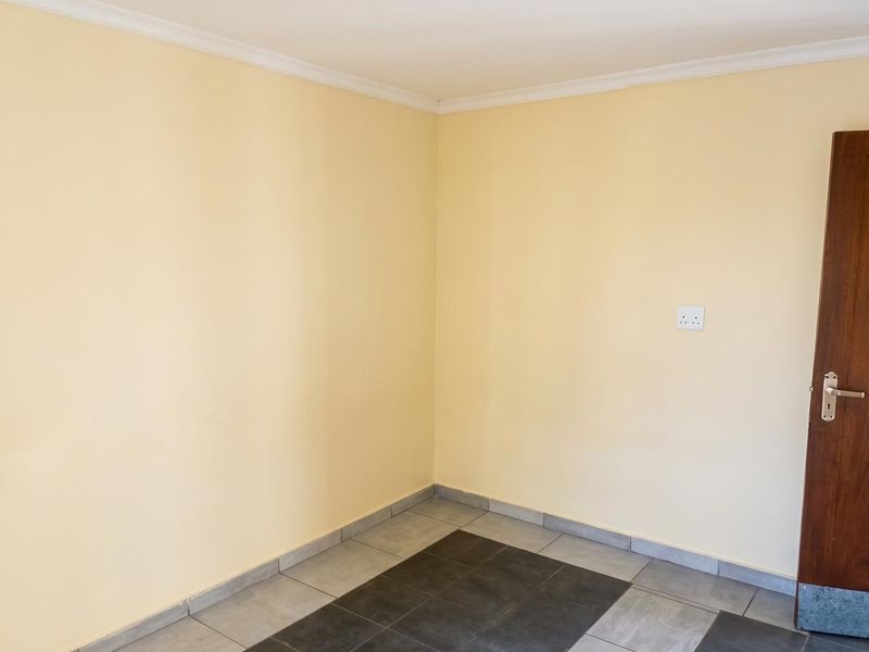 An empty bedroom featuring neutral painted walls, tiled flooring, and a wooden door, providing a blank canvas for personalization.