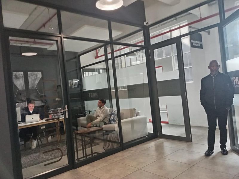 Modern office space featuring glass partition walls, tiled flooring, and an industrial-style exposed ceiling design.