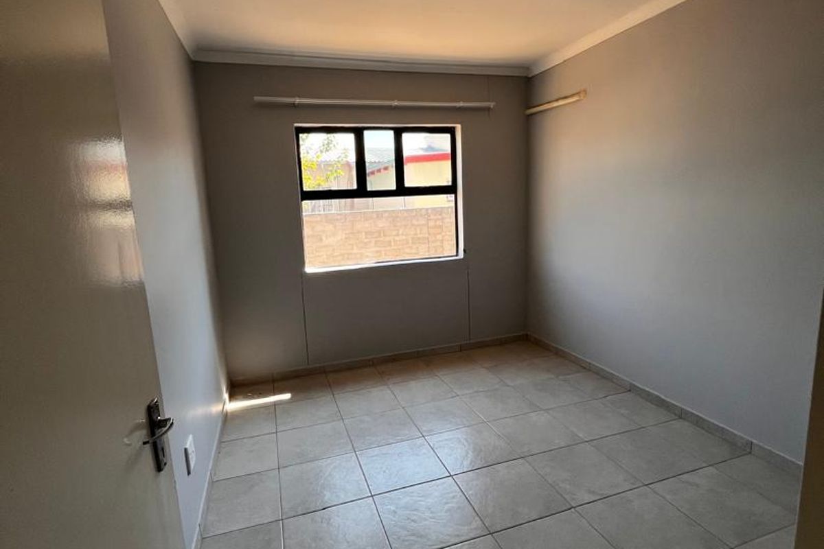 A clean, empty bedroom featuring neutral tiled flooring, a single window with a black frame, and simple ceiling lighting.