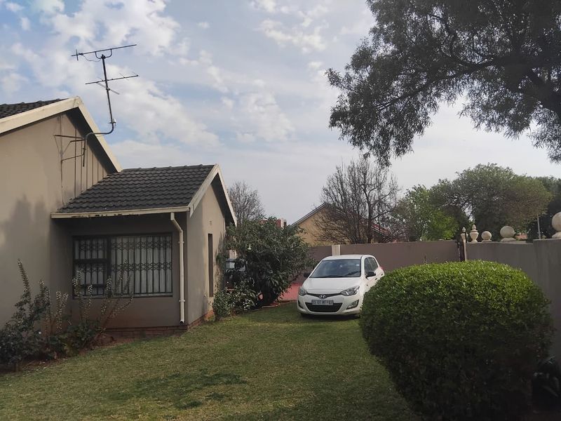 Front view of the house featuring a tiled roof, security bars on windows, and a surrounding boundary wall with a lawn area.