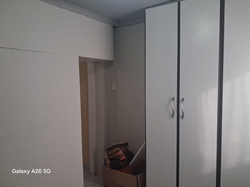 A bedroom interior featuring built-in cupboards with white doors and silver handles, showing signs of dated finishes and basic construction.