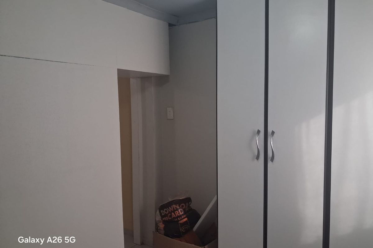 A bedroom interior featuring built-in cupboards with white doors and silver handles, showing signs of dated finishes and basic construction.