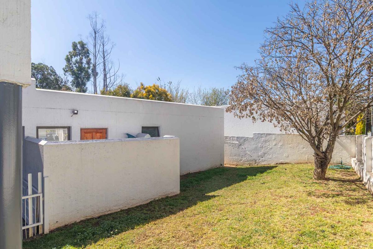 A rear garden area featuring a lawn, mature tree, and perimeter boundary walls with a security gate.