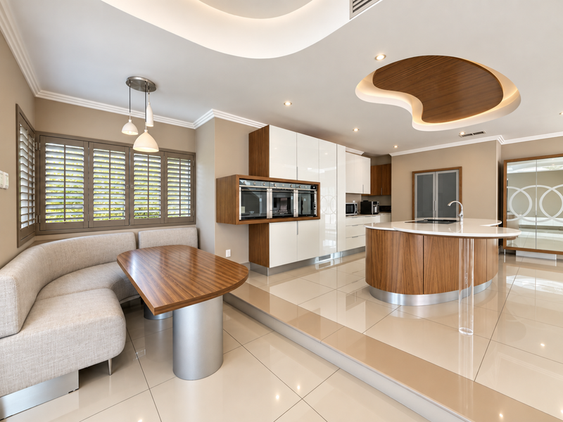 Modern open-plan kitchen and dining area featuring a curved island, high-gloss cabinetry, built-in appliances, and elegant recessed ceiling details.