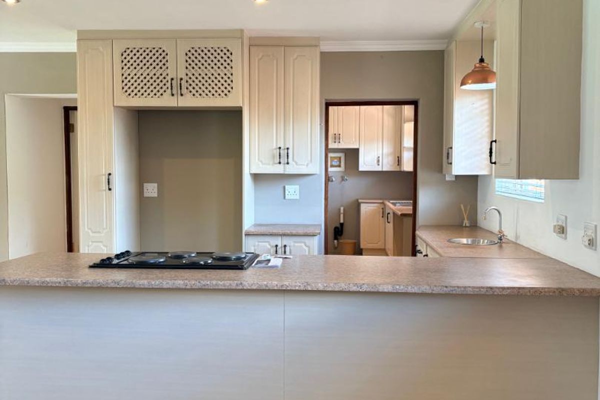 A functional kitchen featuring a breakfast bar, built-in cabinetry, a hob, and an adjacent scullery area with additional storage and sink.