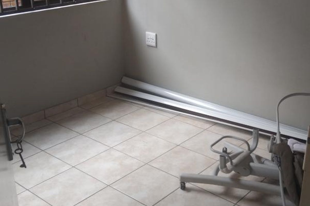 A small, tiled room featuring a window with security bars, suitable for use as a bedroom or home office.