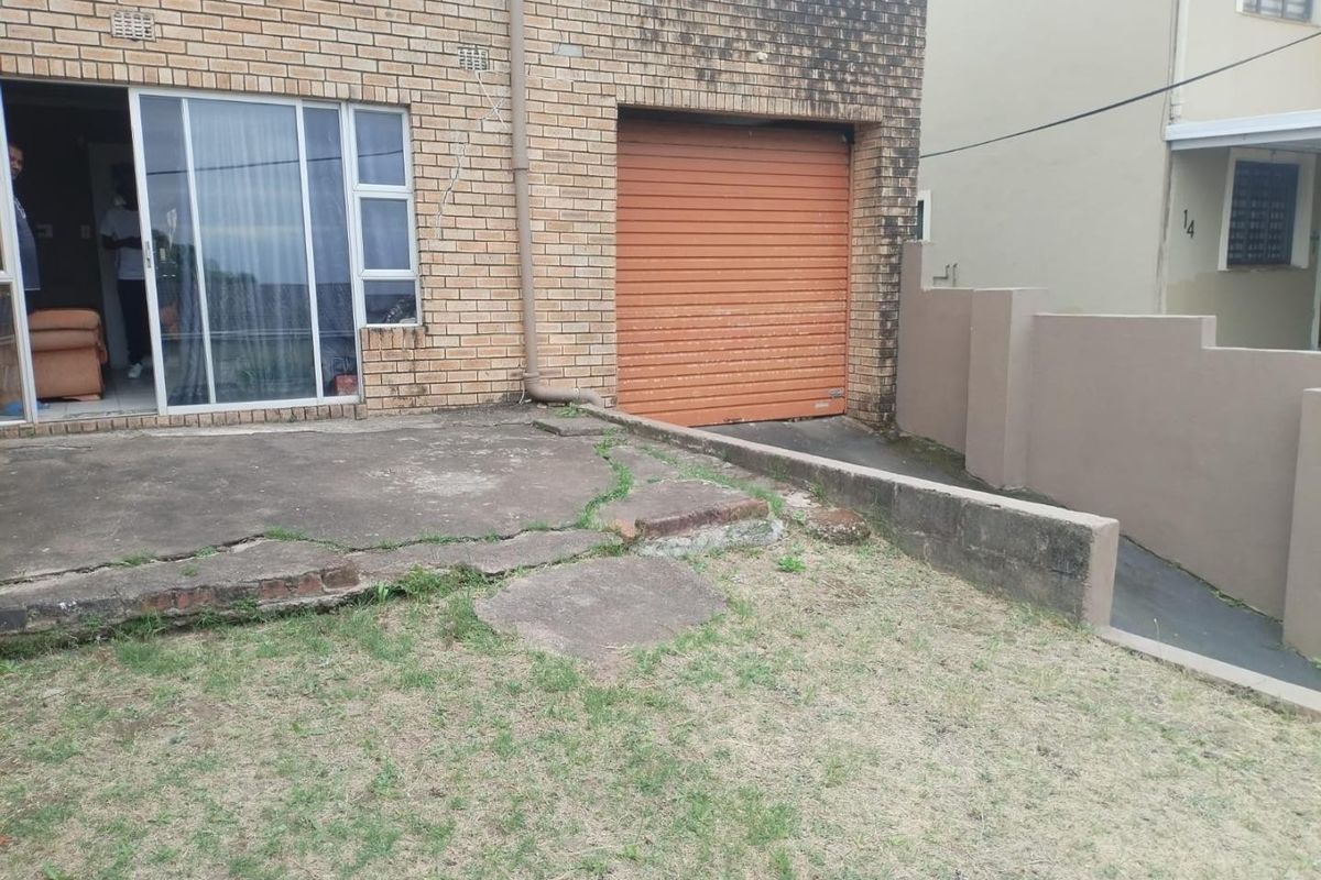 Rear exterior view of the property featuring a brick facade, roller garage door, sliding glass door access, and a concrete patio area.