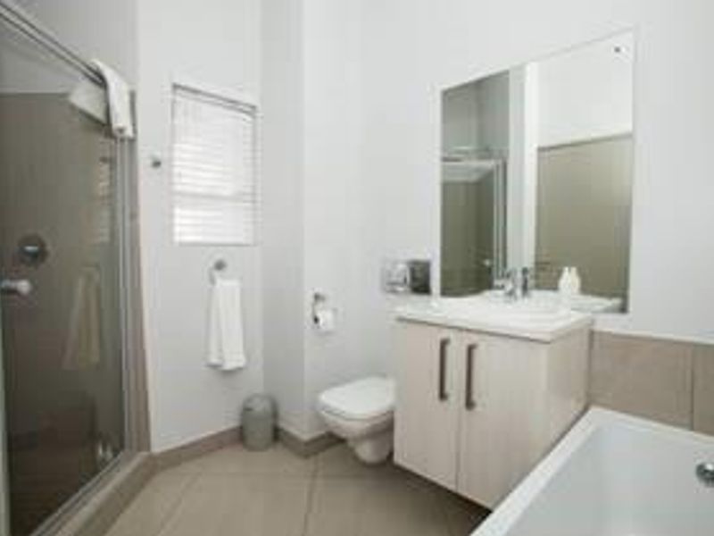 A modern bathroom featuring a glass shower enclosure, wall-mounted toilet, vanity with basin, and a bathtub with neutral tiled finishes.