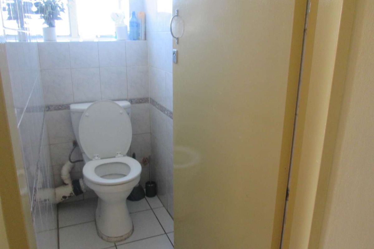 A compact bathroom featuring a standard toilet, tiled walls and flooring, and a window for natural light.