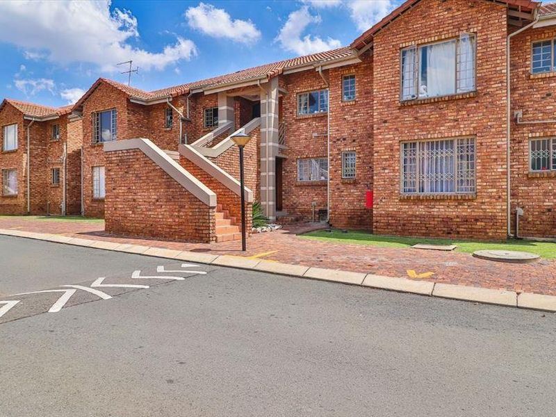 A view of the townhouse complex exterior featuring face brick construction, tiled roofing, and paved access areas with security bars on windows.