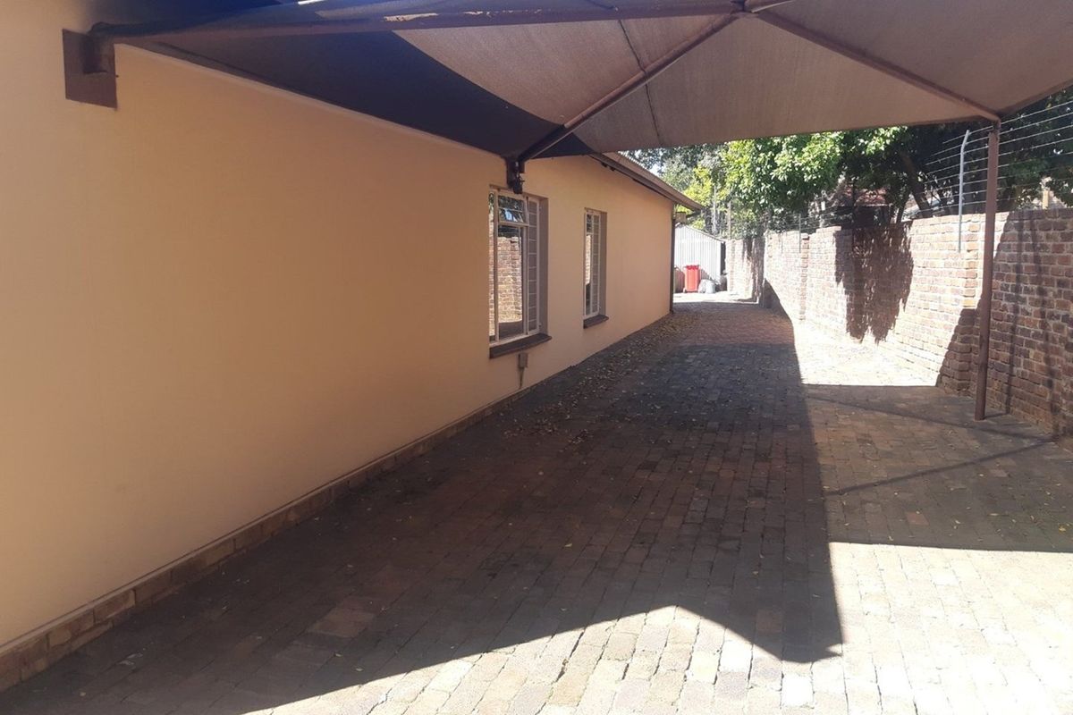 A paved side passage or rear exterior area featuring a shade sail, brick boundary wall, and security-fitted windows.