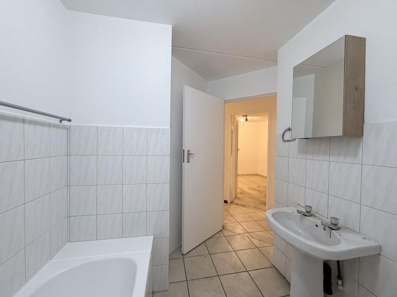 A functional bathroom featuring a bathtub, pedestal sink, and wall-mounted mirror cabinet, finished with tiled flooring and wall splashbacks.