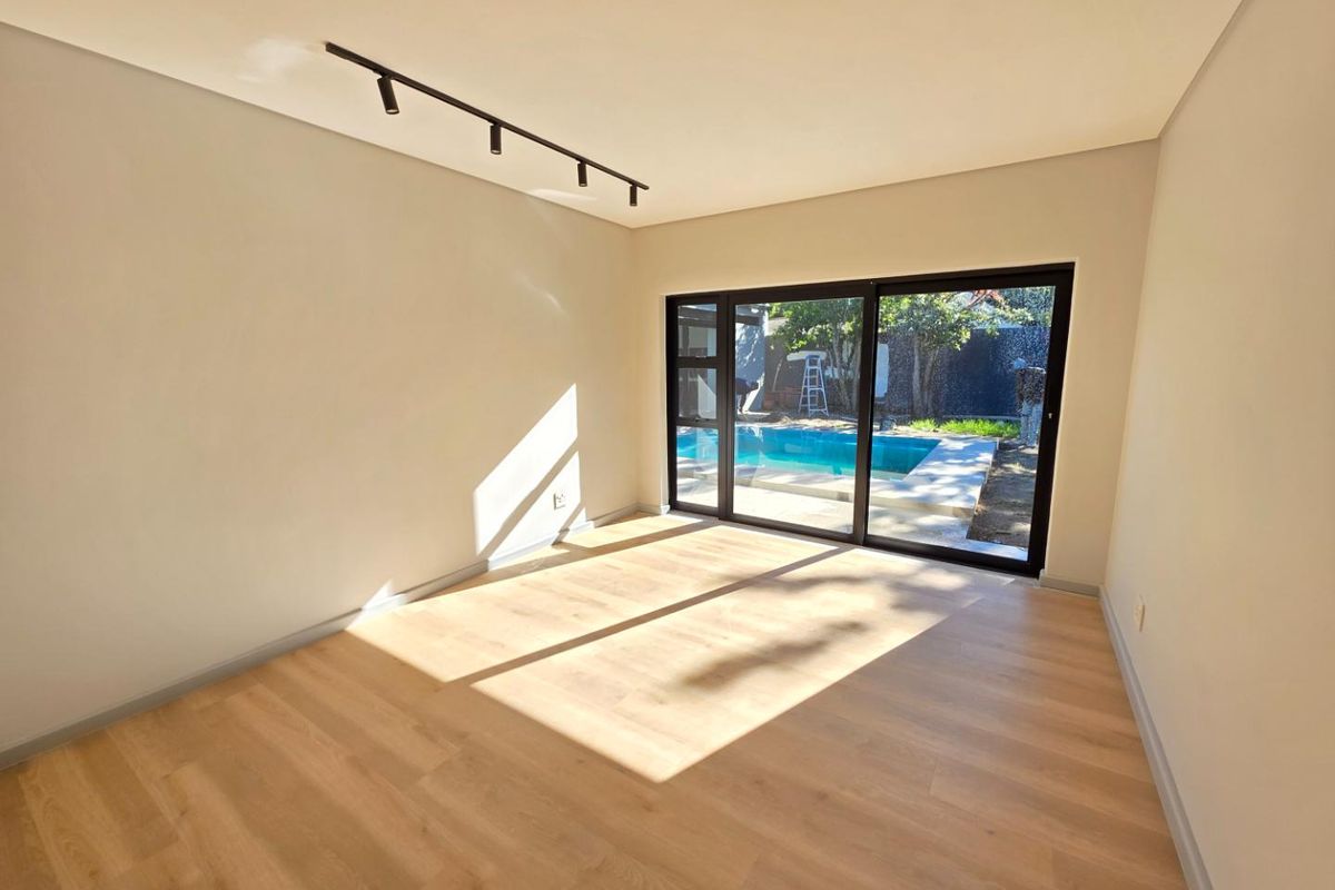 Bright, modern living room featuring light wood-look laminate flooring, sleek track lighting, and large sliding glass doors opening to a pool area.