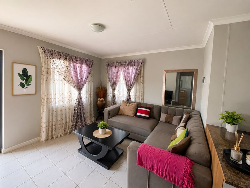A well-maintained living room featuring neutral wall tones, tiled flooring, and ample natural light through dual windows.