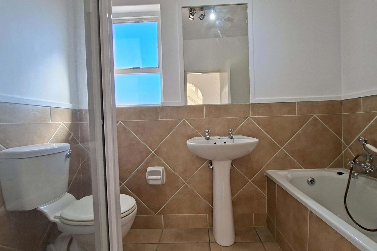 A functional bathroom featuring a pedestal basin, bathtub, and separate shower enclosure with neutral wall tiling and a wall-mounted mirror.