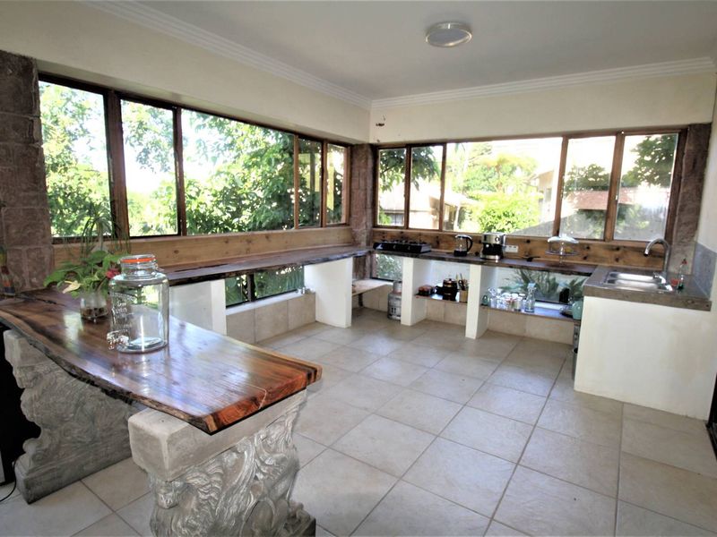 A unique kitchen area featuring custom stone-supported wooden slab countertops, tiled flooring, and expansive windows providing ample natural light and garden views.