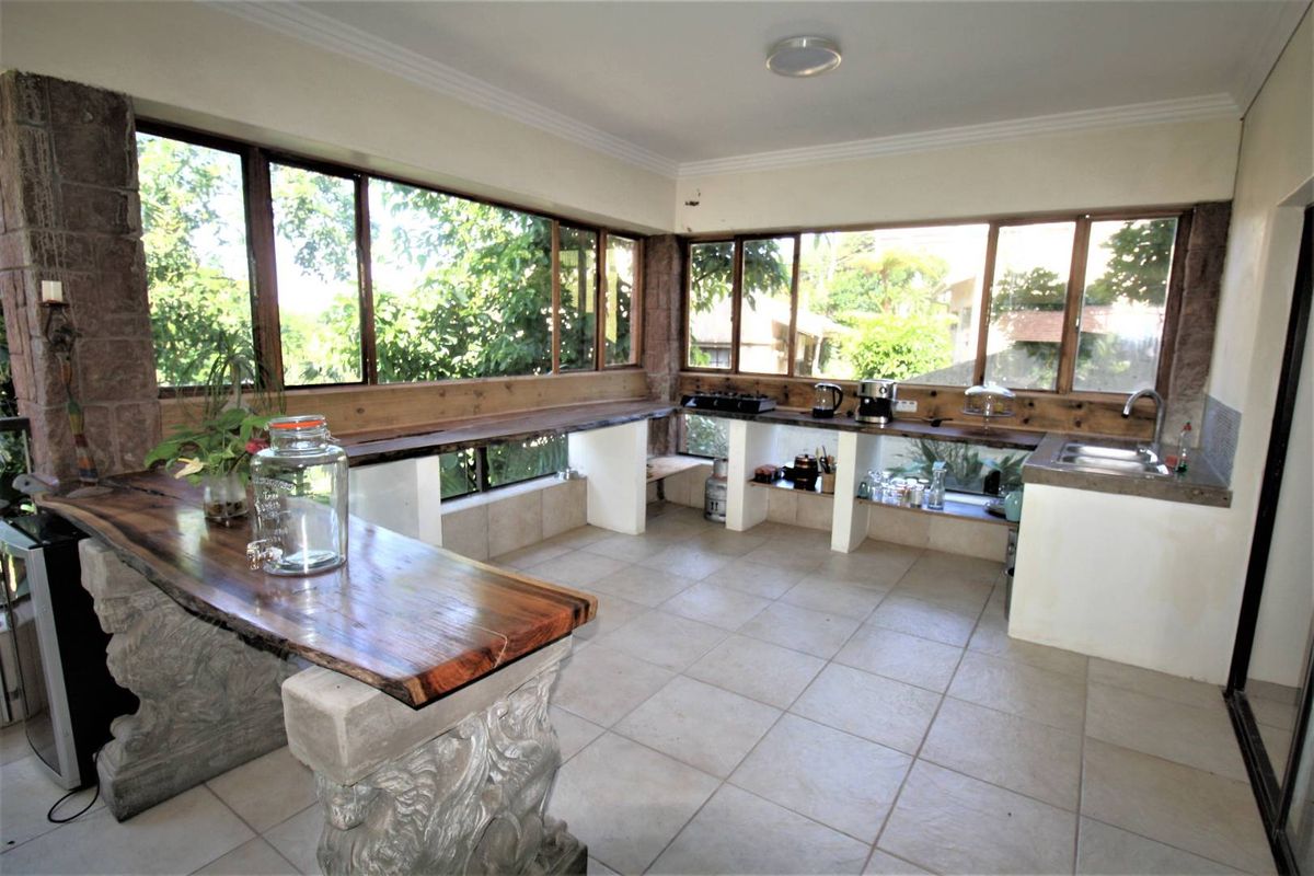A unique kitchen area featuring custom stone-supported wooden slab countertops, tiled flooring, and expansive windows providing ample natural light and garden views.