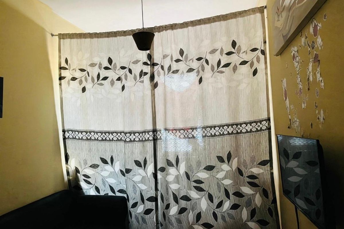 A living room area featuring a curtain-covered window and a central pendant light fixture.