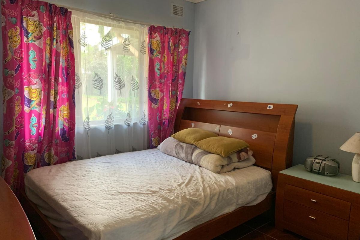 A bedroom featuring tiled flooring and a window with natural light, currently requiring cosmetic updates to the wall finishes.