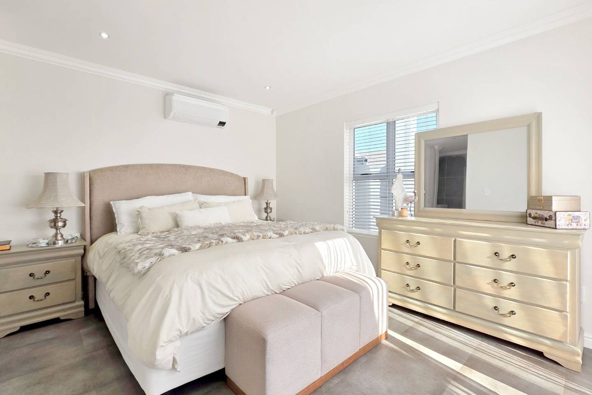 A well-maintained bedroom featuring tiled flooring, recessed downlighting, a wall-mounted air conditioning unit, and large windows with fitted venetian blinds.