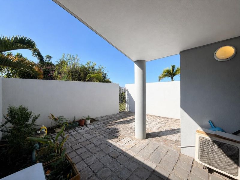 A private, paved outdoor patio area featuring a structural column, perimeter boundary walls, and a metal gate, offering a clean and functional exterior space.