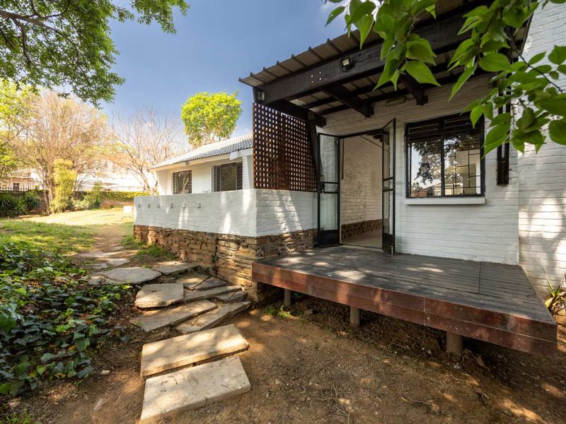 Rear exterior view featuring a raised timber deck, stone cladding, and a stone pathway leading through the garden.