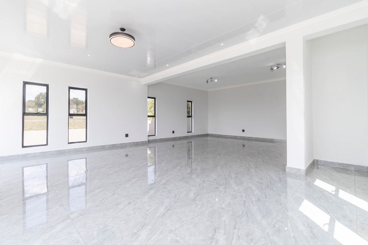 A spacious, bright, and empty living area featuring high-gloss marble-look floor tiles, modern recessed lighting, and large aluminium-framed windows.