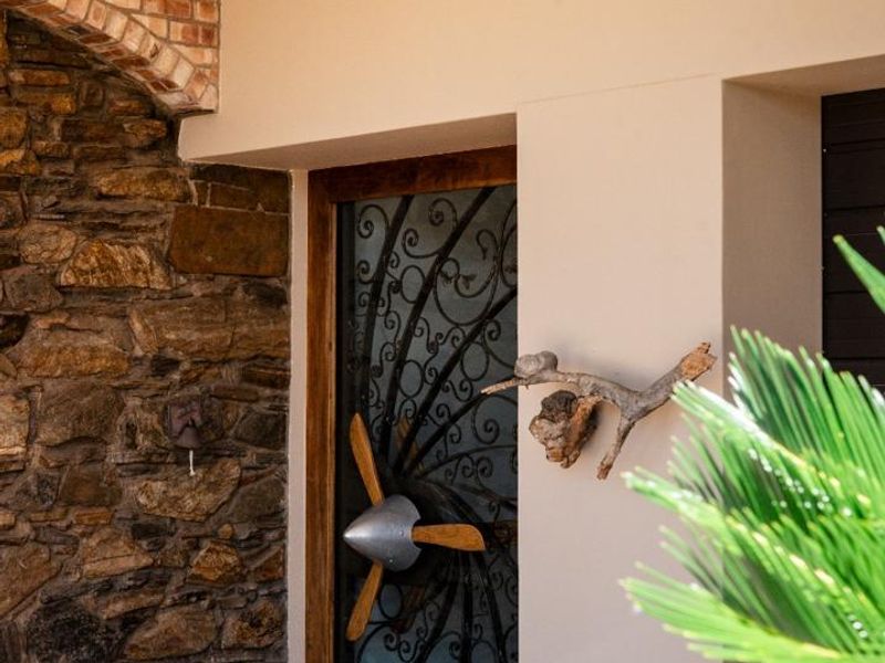A welcoming entrance featuring a decorative wrought iron security gate, rustic stone feature wall, and a brick archway under a covered porch.