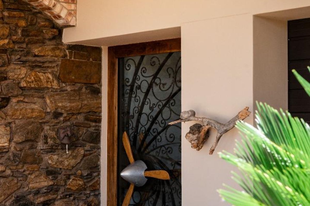 A welcoming entrance featuring a decorative wrought iron security gate, rustic stone feature wall, and a brick archway under a covered porch.