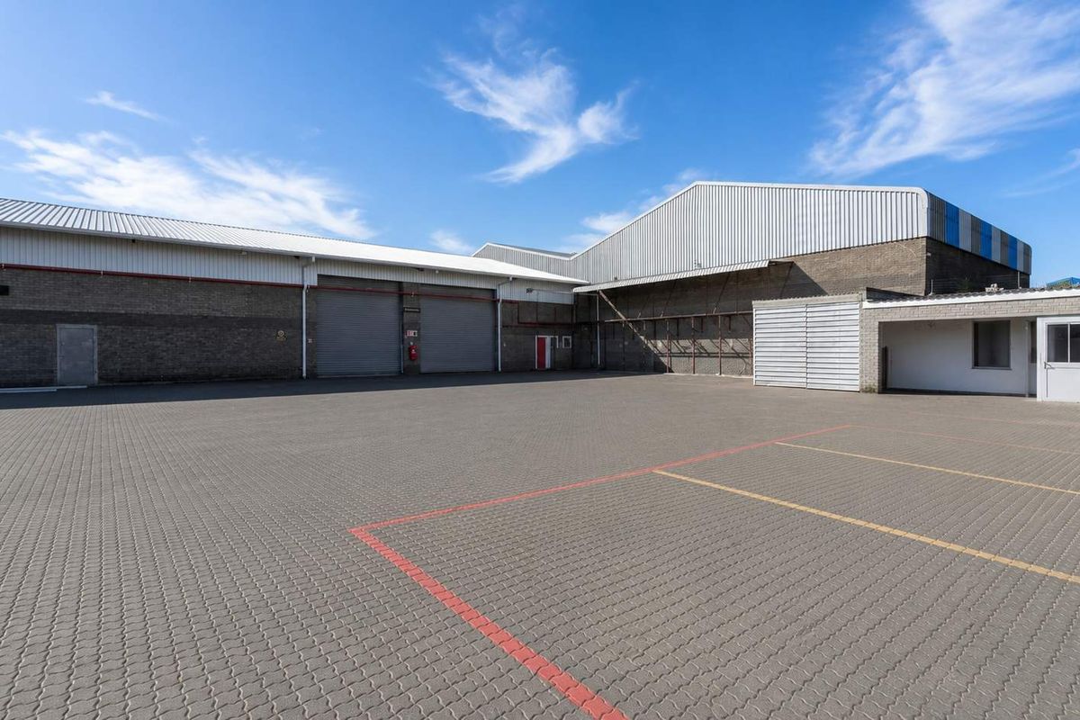Spacious industrial yard featuring paved surfacing, multiple roller shutter doors for loading access, and secure brick-walled warehouse exterior.