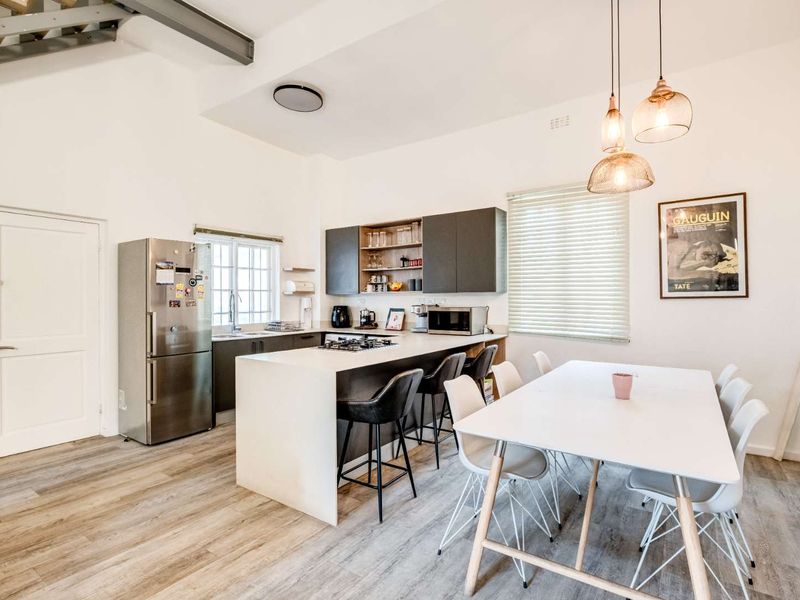 Modern open-plan kitchen and dining area featuring a central island with integrated cooktop, sleek cabinetry, and light wood-look laminate flooring.