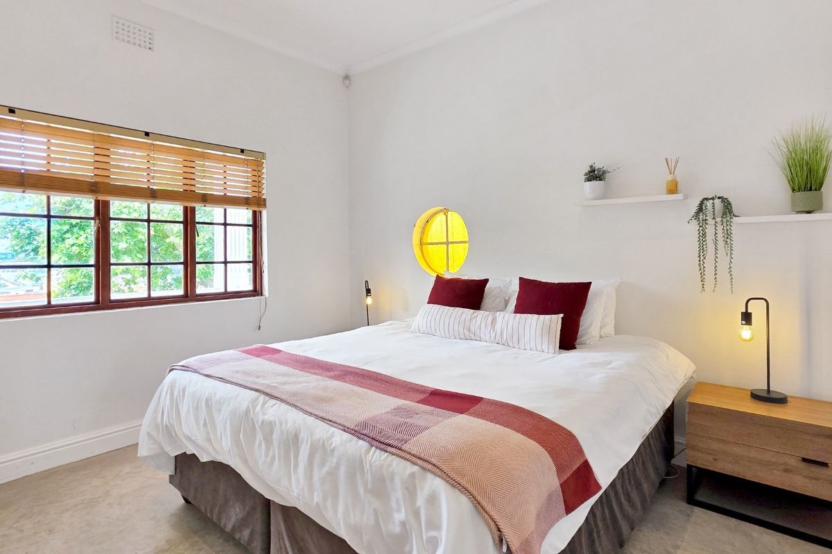 A bright bedroom featuring a timber-framed window with blinds and a unique circular accent window, finished with neutral walls and recessed lighting.