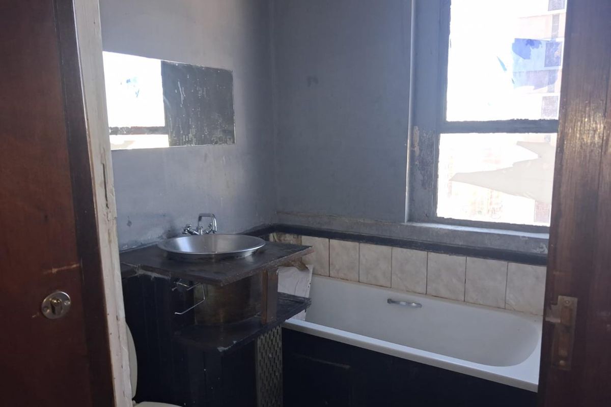 A dated bathroom featuring a vessel sink, bathtub, and tiled splashback, currently in need of significant renovation and repair.