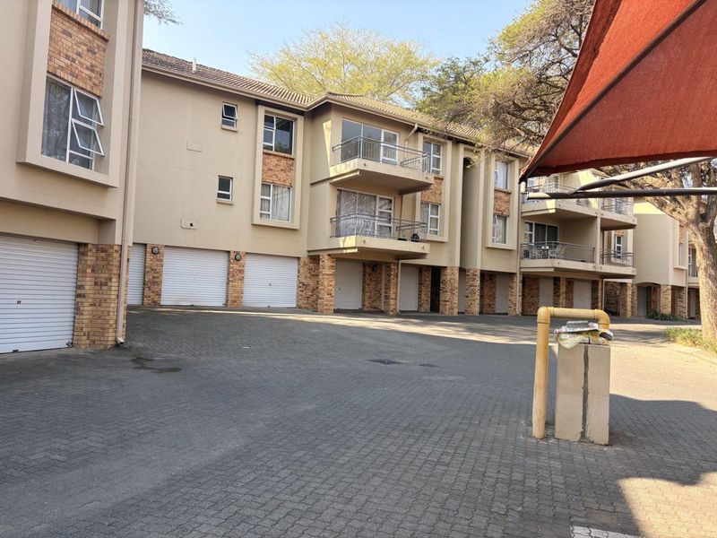 Exterior view of a multi-story apartment complex featuring brick and plaster facade, private balconies, and ground-level garage access with paved driveway.