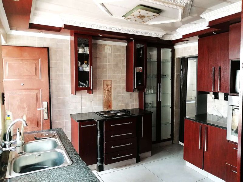 A functional kitchen featuring dark wood cabinetry, granite countertops, a double sink, and built-in appliances with decorative ceiling detailing.