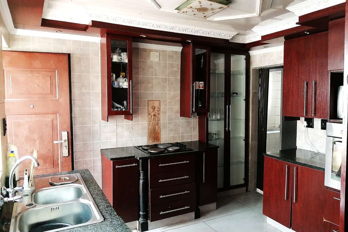 A functional kitchen featuring dark wood cabinetry, granite countertops, a double sink, and built-in appliances with decorative ceiling detailing.