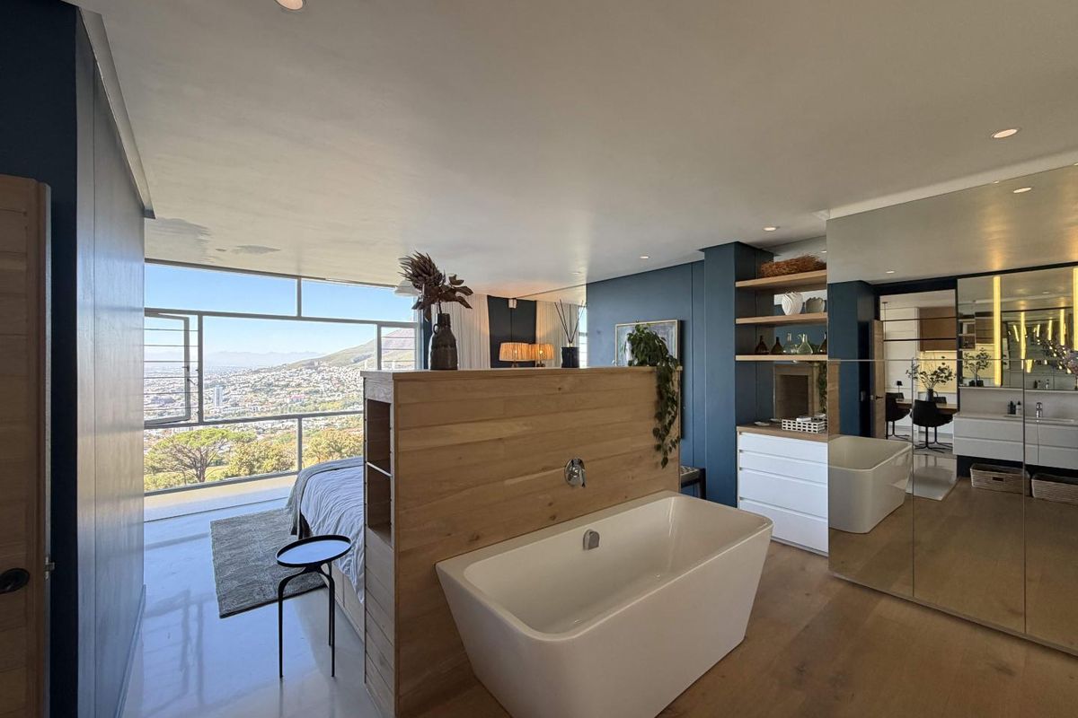 Modern open-plan bedroom suite featuring a freestanding bathtub, integrated timber partition, built-in shelving, and expansive floor-to-ceiling windows with panoramic city views.