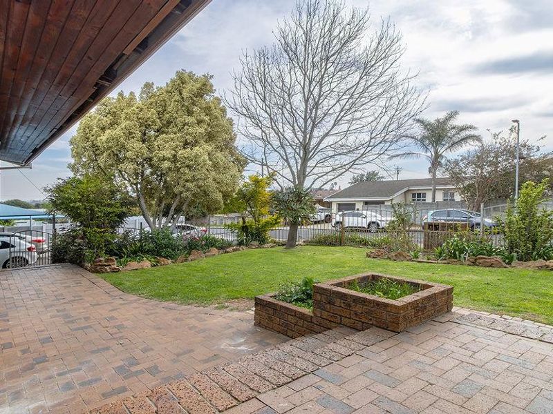 A covered brick-paved patio area overlooking a landscaped garden with a raised brick planter box and secure perimeter fencing.