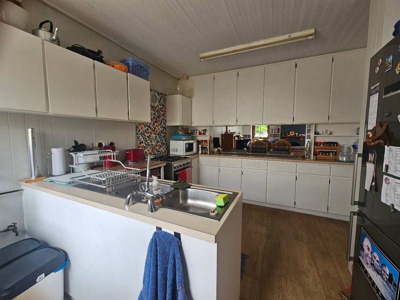 A functional kitchen featuring extensive built-in cabinetry, a stainless steel sink, and a tiled backsplash, offering a dated aesthetic ready for modernization.