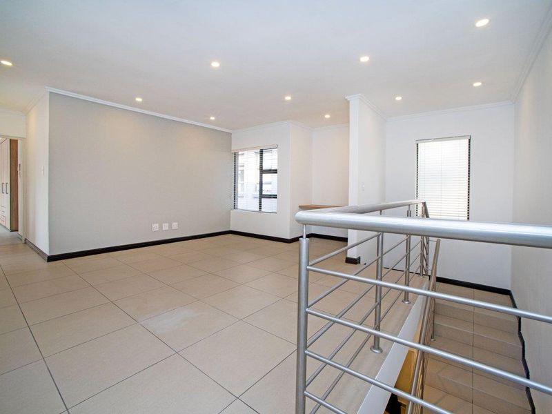 An open-plan living area featuring neutral tiled flooring, recessed downlights, a stainless steel balustrade, and a convenient built-in desk nook.